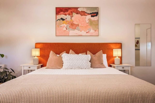 A hotel room with a large bed, two bedside tables with lamps, a painting on the wall, and a mirror on the wall.