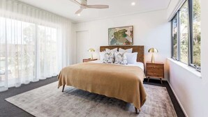 Een slaapkamer met een bed, een plafondventilator, een raam en een nachtkastje met een lamp.