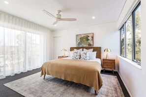 Une chambre à coucher avec un lit, un ventilateur de plafond, une fenêtre et une table de chevet avec une lampe.