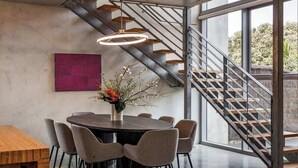 Een moderne eetruimte met een ronde tafel, stoelen, een vaas met bloemen, een trap en een groot raam.
