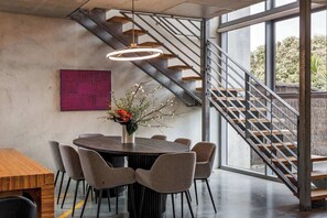 Un espace de salle à manger moderne avec une table ronde, des chaises, un vase de fleurs, un escalier et une grande fenêtre.