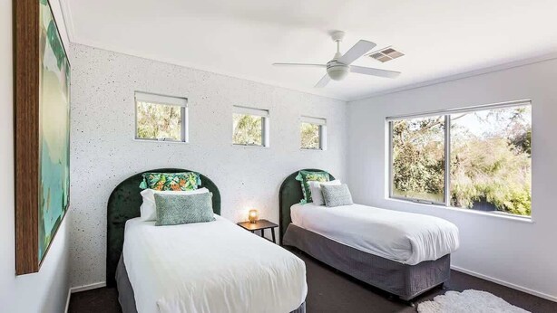 Une chambre avec deux lits, un ventilateur de plafond et une grande fenêtre.