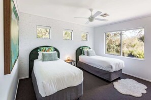 Een slaapkamer met twee bedden, een plafondventilator en een groot raam.
