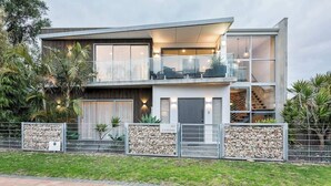 Een modern huis met twee verdiepingen, een balkon, grote ramen en een stenen muur aan de voorzijde.