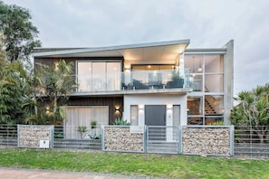 Une maison moderne à deux étages, dotée d’un balcon, de grandes fenêtres et d’un mur en pierre à l’avant.