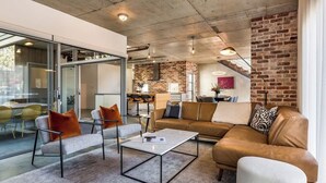 Un salon moderne doté d’une cloison en verre, d’un canapé en cuir marron, d’une table basse blanche et d’un mur décoratif en briques.