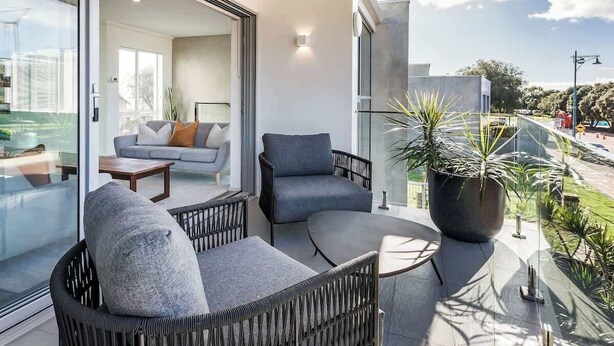 Een modern balkon met rieten meubels, een grote potplant en een glazen deur naar een woonruimte.