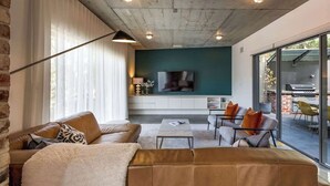 Un salon moderne doté d’un grand téléviseur, de sièges confortables et offrant une vue sur l’extérieur.