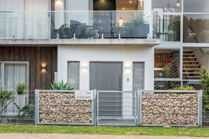 Een modern, twee verdiepingen hoog gebouw met een balkon, een stenen muur en een bord met het adres.