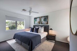 Un dormitorio moderno con cama, ventilador de techo, ventana y obras de arte en la pared.