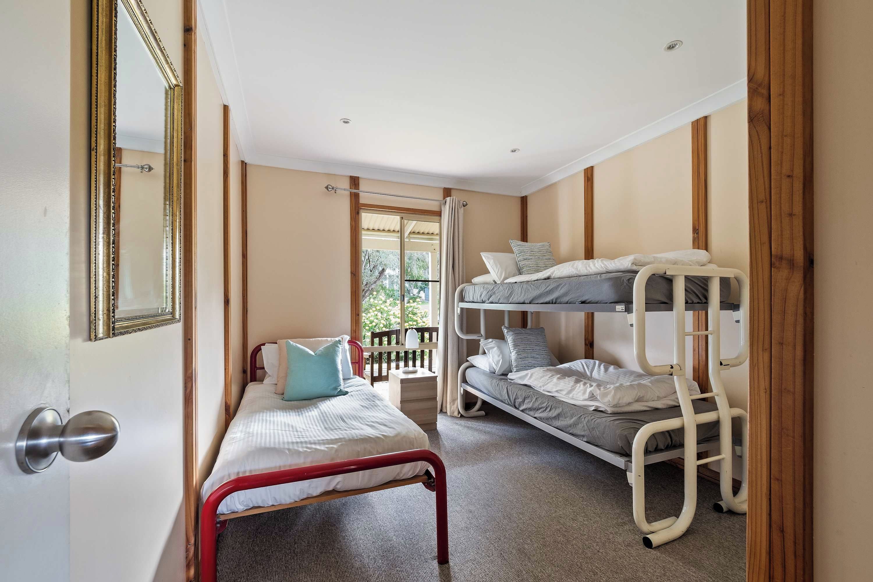 A room with bunk beds, a single bed, a wooden door, and a mirror.