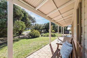 Ein überdachter Patio-Bereich mit Tisch und Stühlen, umgeben von einem Garten mit verschiedenen Pflanzen und Bäumen.