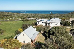 Een kustwoning met een groot huis, zonnepanelen en uitzicht op de oceaan.