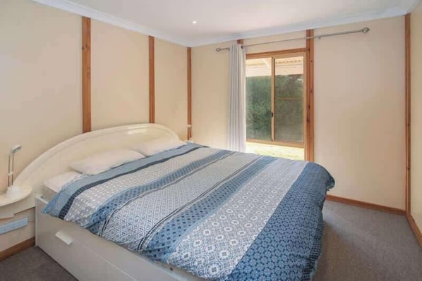 Une chambre à coucher avec un lit, une table de chevet, une fenêtre avec des rideaux et une vue sur la verdure à l’extérieur.