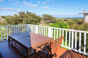 Une terrasse en bois, agrémentée d’une table et de chaises, entourée d’une balustrade blanche, et offrant une vue sur un paysage naturel.