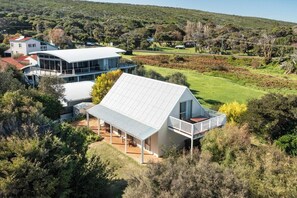 Une maison moderne dotée d’une grande façade vitrée, d’un patio couvert et offrant une vue sur le paysage environnant.