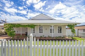 A single-story house with a gabled roof, a covered porch, and a white picket fence.