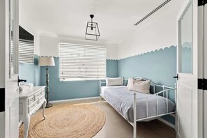 Ein Schlafzimmer mit Bett, Kommode, Lampe und einem Fenster mit Jalousien.