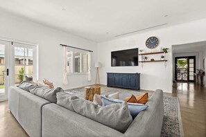 Ein Wohnzimmer mit grauem Sofa, einem an der Wand montierten Fernseher und einem Holzschrank.