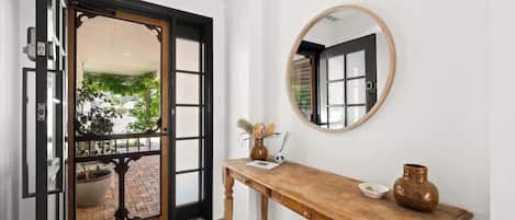 A hallway with a wooden console table, a round mirror, and a door leading to an outdoor area with potted plants.