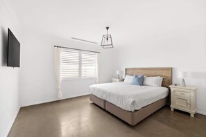 A bedroom with a bed, bedside tables, a TV, and a window with blinds.