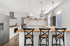 Eine moderne Küche mit weißen Schränken, einer Holzinsel, schwarzen Barhocker, Pendelleuchten und einem Edelstahl-Kühlschrank.