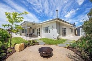 A modern house with a covered patio, a fire pit, and a well-maintained garden.