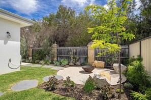 A backyard with a concrete patio, a fire pit, and various plants.