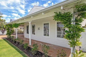 A single-story house with a covered porch, a small garden with various plants, and a clear sky.