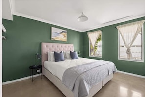 Une chambre à coucher avec un grand lit, une table de chevet, un tableau au mur et une fenêtre avec des rideaux.
