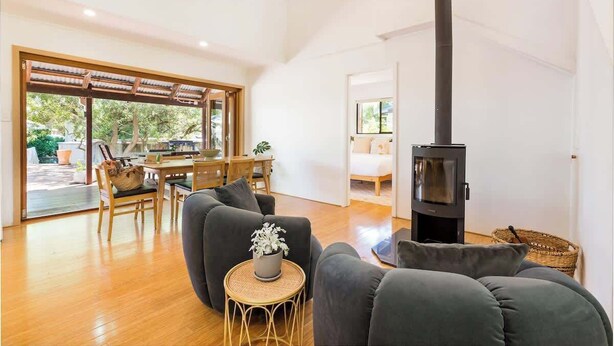 A spacious living area with a sofa, a small round table, a fireplace, and a dining area with a table and chairs. - Mika Cabin—Breezy Family Haven, Easy Walk to Beach (Eagle Bay)