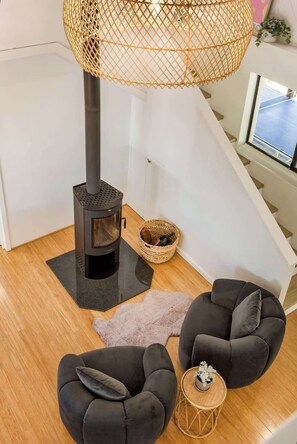 A modern living room with a wood-burning stove, two black sofas, a woven lamp, and a small table with a plant.