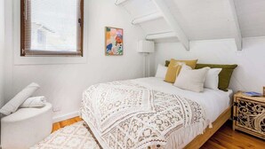 A bedroom with a bed, a window with blinds, a bedside table, and a wall-mounted lamp. - Mika Cabin—Breezy Family Haven, Easy Walk to Beach (Eagle Bay)