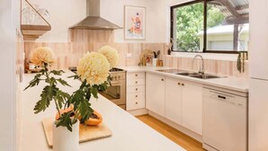 A modern kitchen with white cabinetry, a stainless steel sink, and a window with a view of greenery. - Mika Cabin—Breezy Family Haven, Easy Walk to Beach (Eagle Bay)