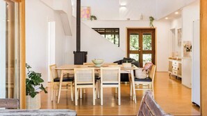 A modern dining area with a wooden table and chairs, a black stove, and a view of the outdoors. - Mika Cabin—Breezy Family Haven, Easy Walk to Beach (Eagle Bay)