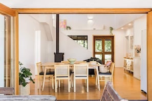 A modern dining area with a wooden table and chairs, a black stove, and a view of the outdoors. - Mika Cabin—Breezy Family Haven, Easy Walk to Beach (Eagle Bay)