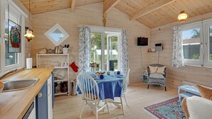 A cozy cabin-style room with a wooden interior, a dining table set for two, a kitchen area with a sink and appliances, and large windows offering views of the outdoors. - Awesome home in Kalundborg with WiFi (Kalundborg)