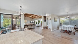 A spacious kitchen with a marble countertop, wooden dining table, and chairs. There is a large window providing a view of the outdoors. - Easy Beach Access, Spacious Decks & Striking Ocean Views - Harris Beach Overlook (Brookings)