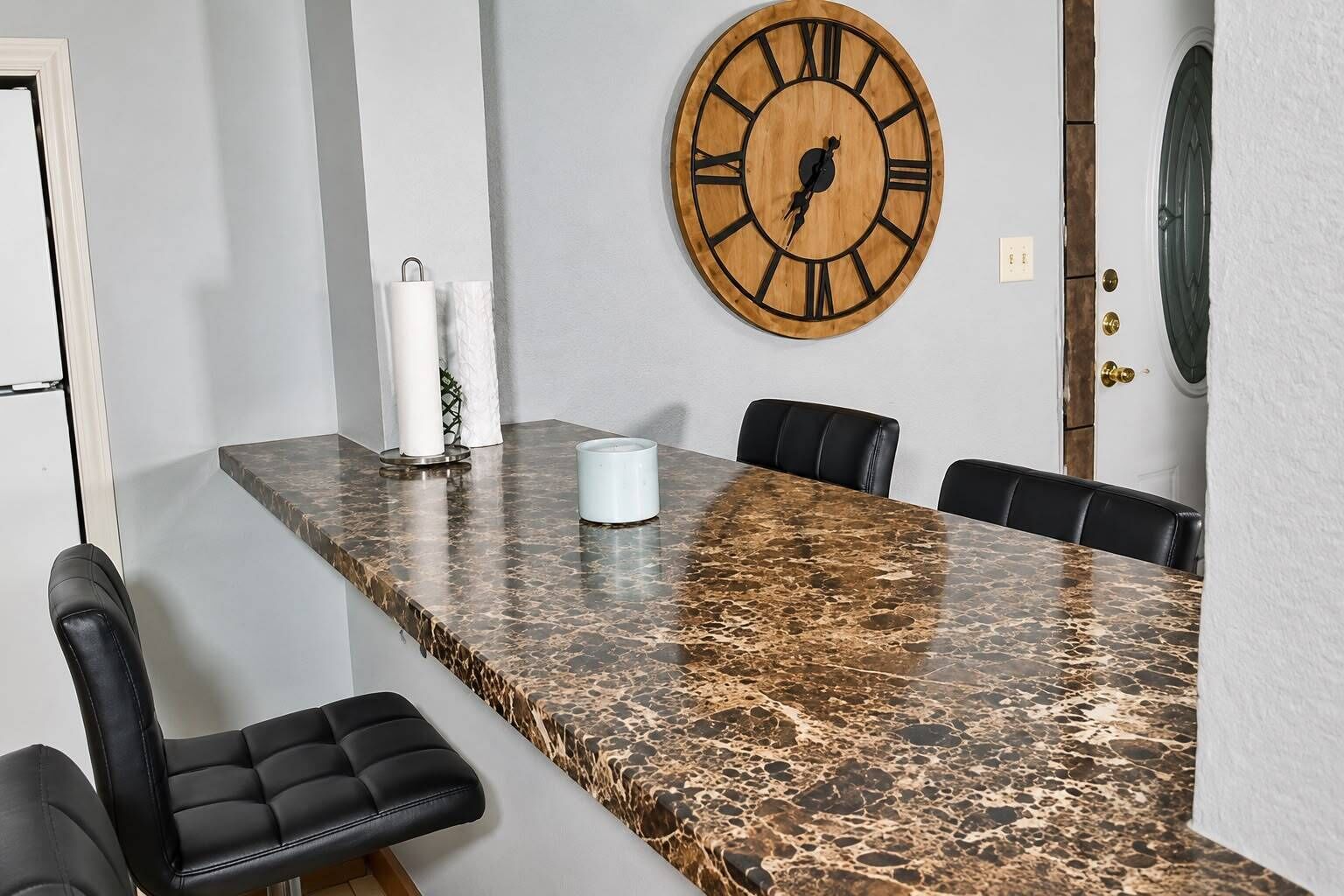 A conference room with a marble table, black leather chairs, and a wooden clock on the wall.