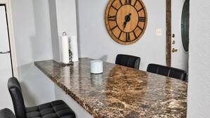 Un salón de conferencias con una mesa de mármol, sillas de cuero negro y un reloj de madera en la pared.