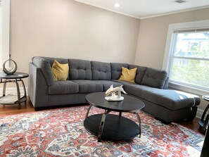 A modern living room with a grey sectional sofa, a round coffee table, and a patterned rug.