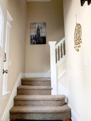 A staircase with carpeted steps, a white railing, and a painting of a building on the wall. - Newly Renovated Spacious 4BR peaceful downtown Apt (Montclair)