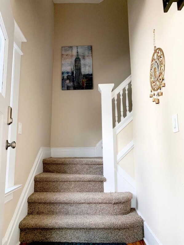 A staircase with carpeted steps, a white railing, and a painting of a building on the wall.