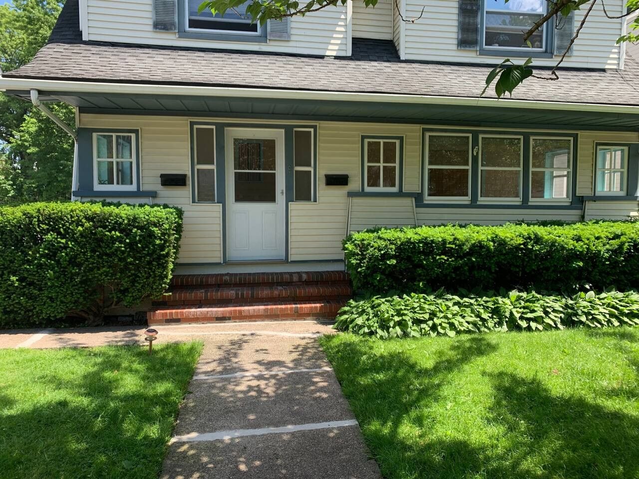 A two-story house with a front porch, a small front yard, and a pathway leading to the door.