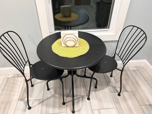 A round black table with a yellow placemat, surrounded by four black metal chairs.