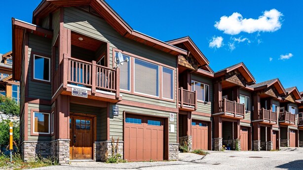 A multi-story building with a prominent balcony, a garage, and a stone foundation. - Bear's Paw Chalet - Amazing Location & Ski In/out (Beaverdell)