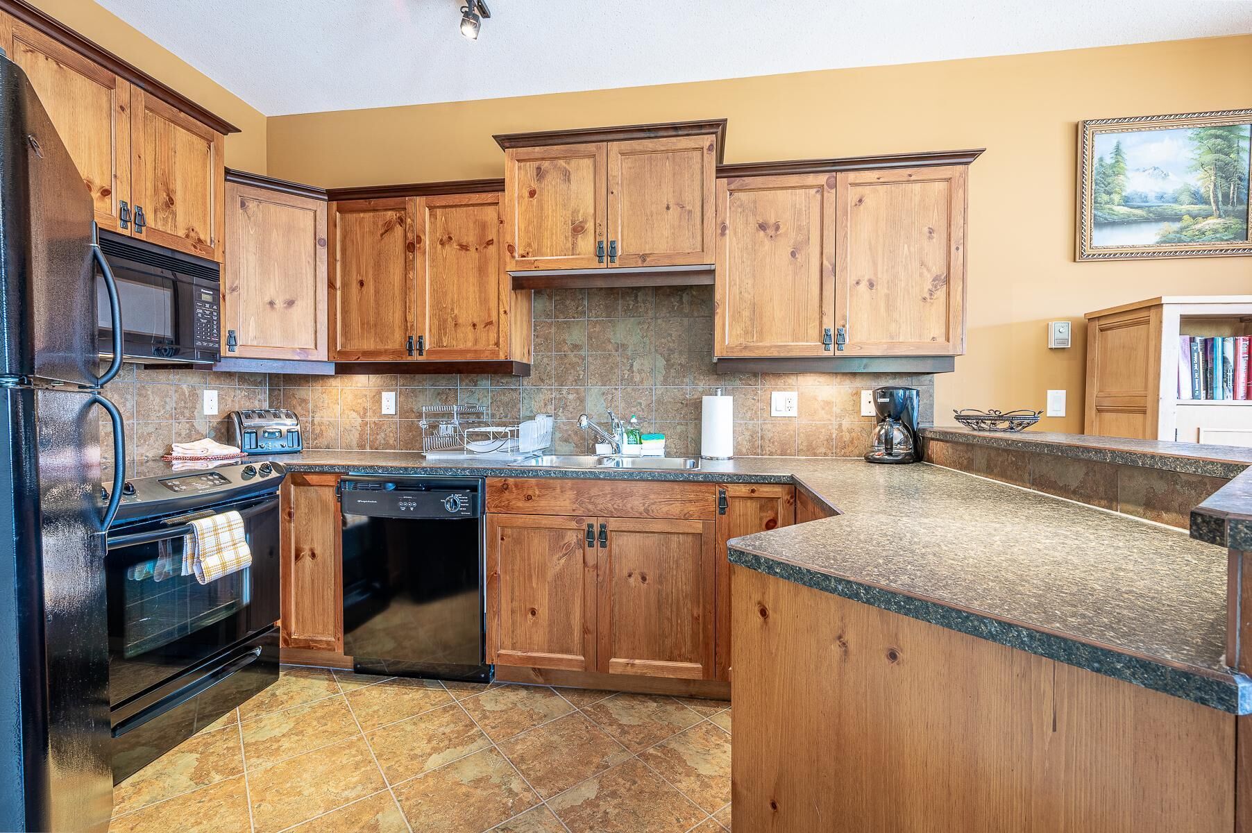 A kitchen with wooden cabinets, a black refrigerator, a microwave, a stove, and a dishwasher.