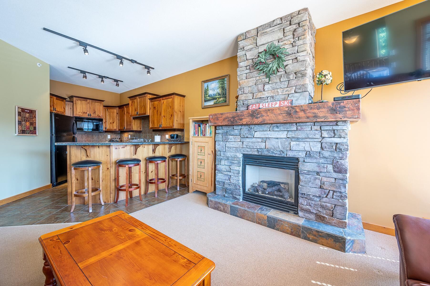 A modern kitchen with wooden cabinets, a stone fireplace, and a bar area with stools.