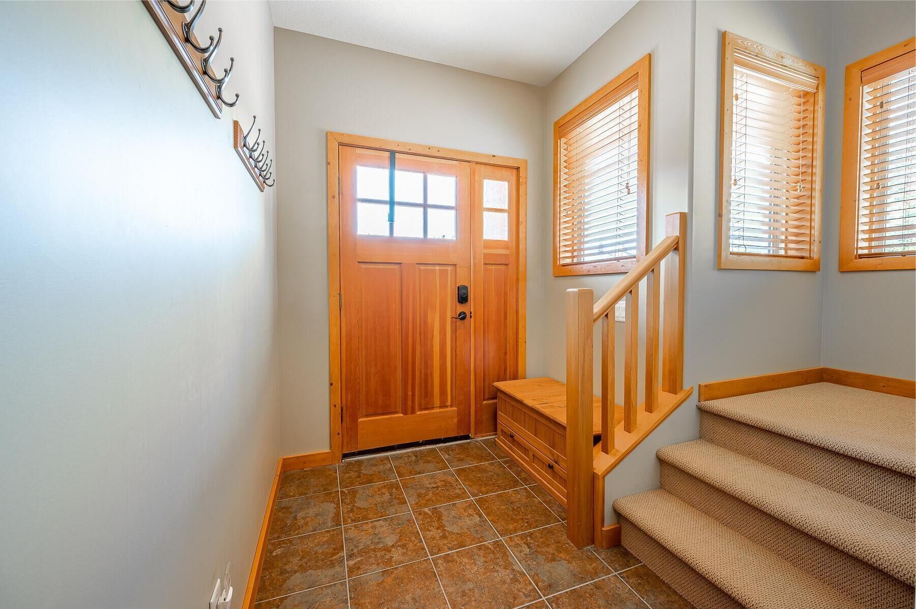 A wooden staircase with a handrail, a wooden door with a window, and a wall-mounted light fixture.