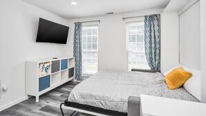 Une chambre à coucher comprenant un lit, un téléviseur fixé au mur, une table de chevet et une armoire avec des tiroirs.